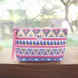 NFI Essentials cosmetic pouch featuring pink, blue, and yellow geometric tribal pattern with a pink wrist strap and zipper.